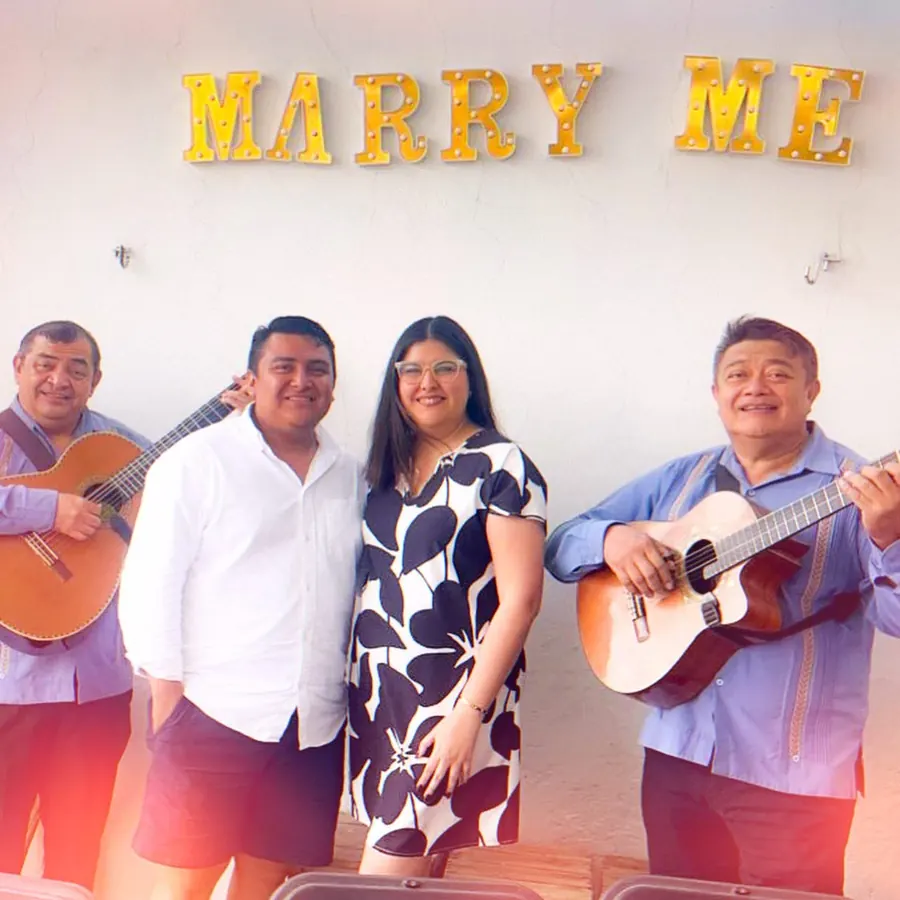 Dariana y Erick con el trío bajo el letrero Marry Me